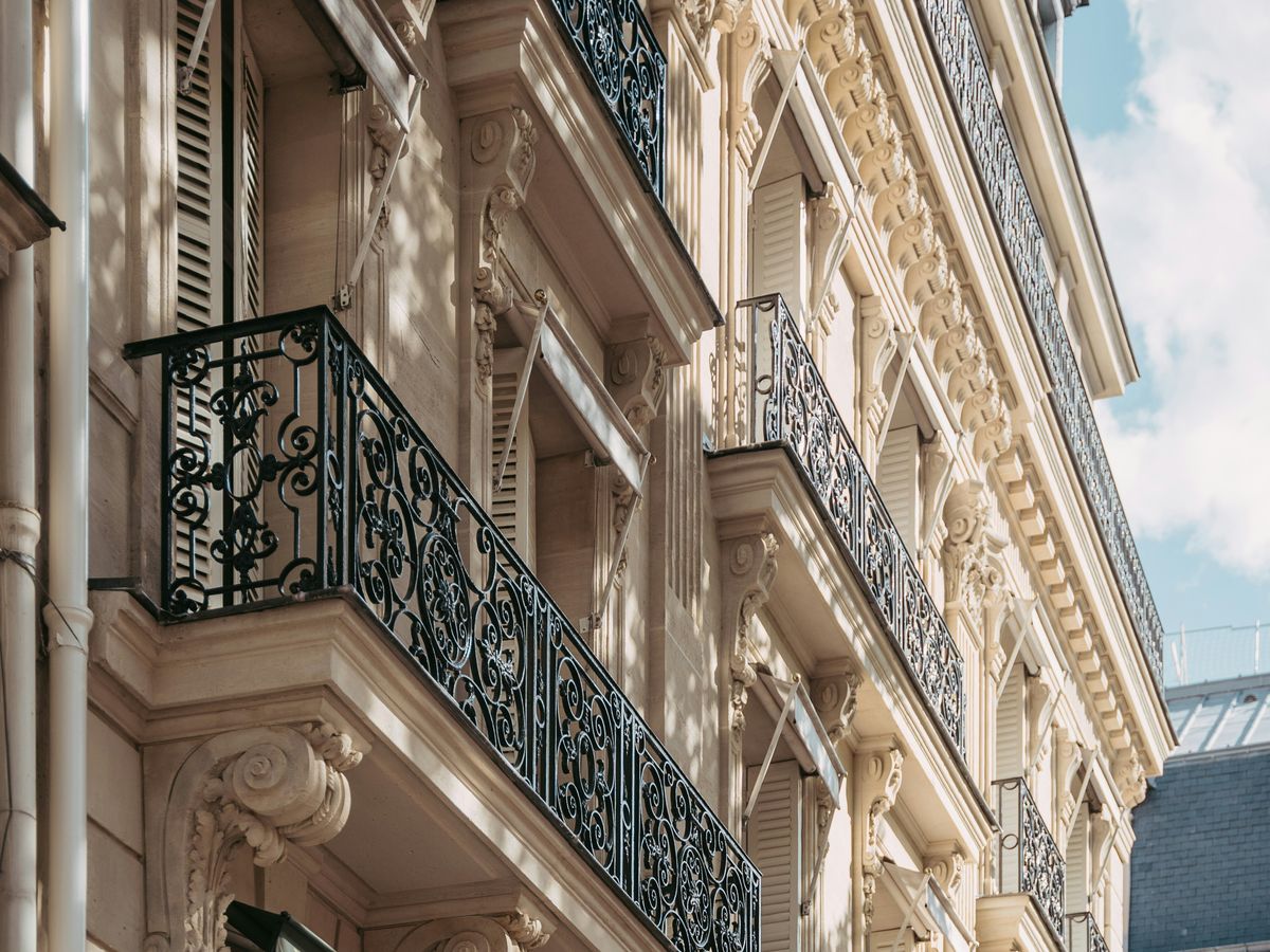 Balcons en ferronnerie ouvragée et corniches sculptées d'une façade haussmannienne, vus en contre-plongée sous la lumière du jour.